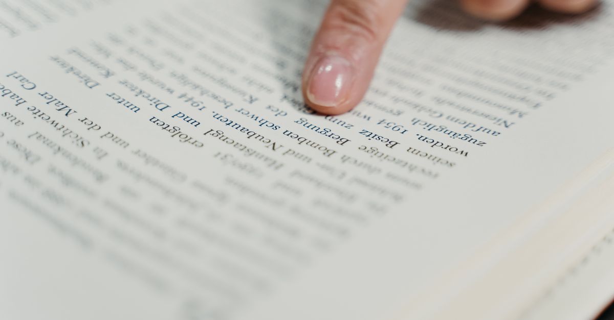 A detailed view of a finger pointing at text in a book, emphasizing reading and study.